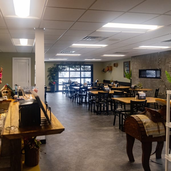 Spacious restaurant dining room with wooden tables, black chairs, a service counter, and a modern fireplace.