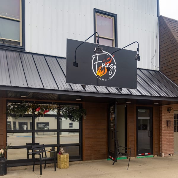 Fuego on Main restaurant exterior with a black sign, wood siding, large glass window, and outdoor seating.