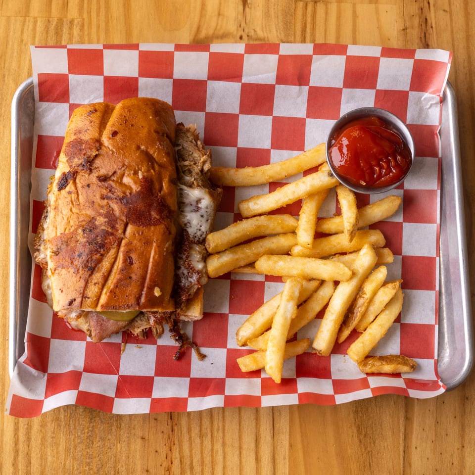 Toasted pulled pork sandwich with melted cheese, fries, and ketchup on a checkered tray.