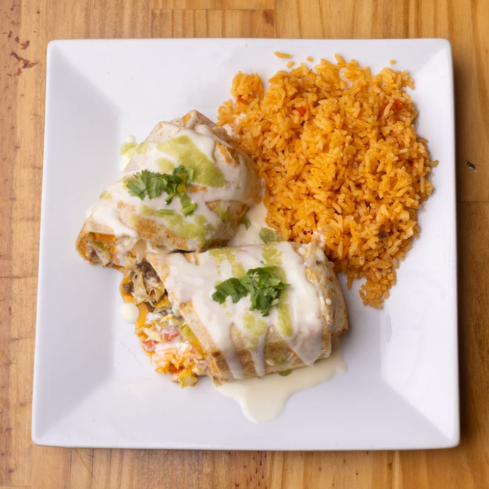 Two sauced burritos with cilantro and orange rice on a white plate, with a fly nearby.