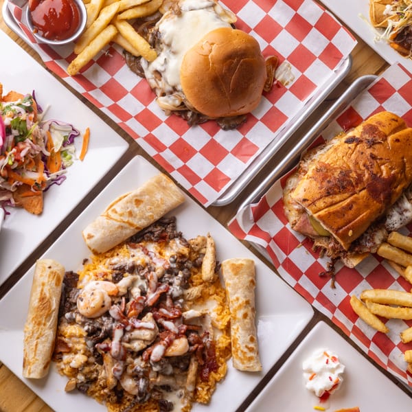 Table spread with various restaurant dishes including burgers, sandwiches, fries, and rice with toppings.