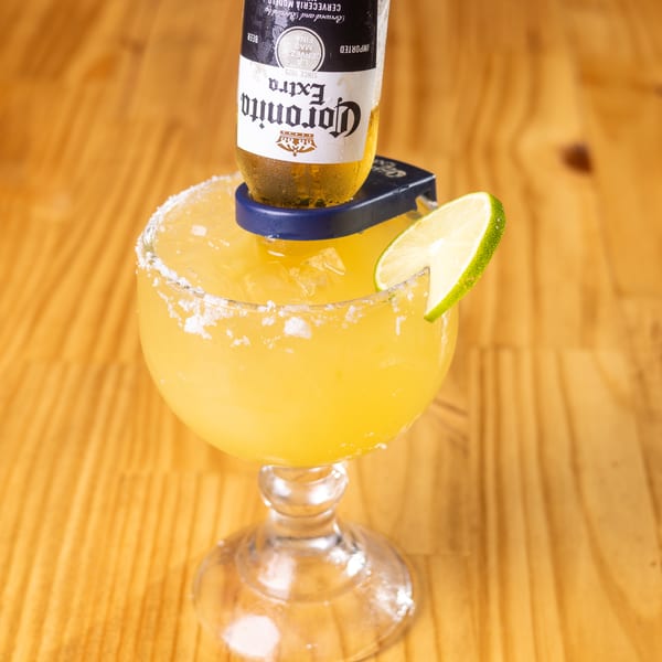 Margarita glass with an inverted Corona Extra beer bottle, a lime wedge, and salted rim on a wooden table.